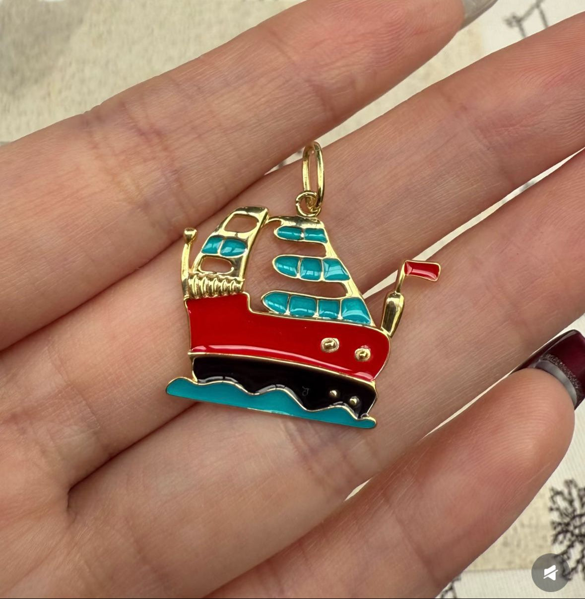 Colorful ship-shaped pendant held between fingers against a floral-patterned background